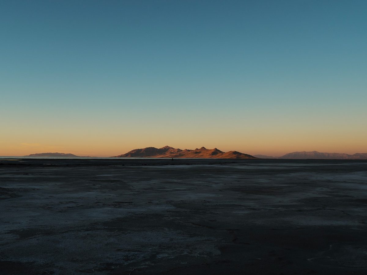 Salt flats at dusk with a sunlit mountain on the horizon under a clear teal sky, edited with Fujifilm Profiles