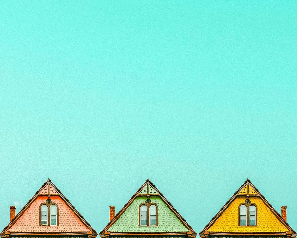 Three pointed rooftops in pink, green and yellow against a clear turquoise sky, edited with the Wes Anderson presets