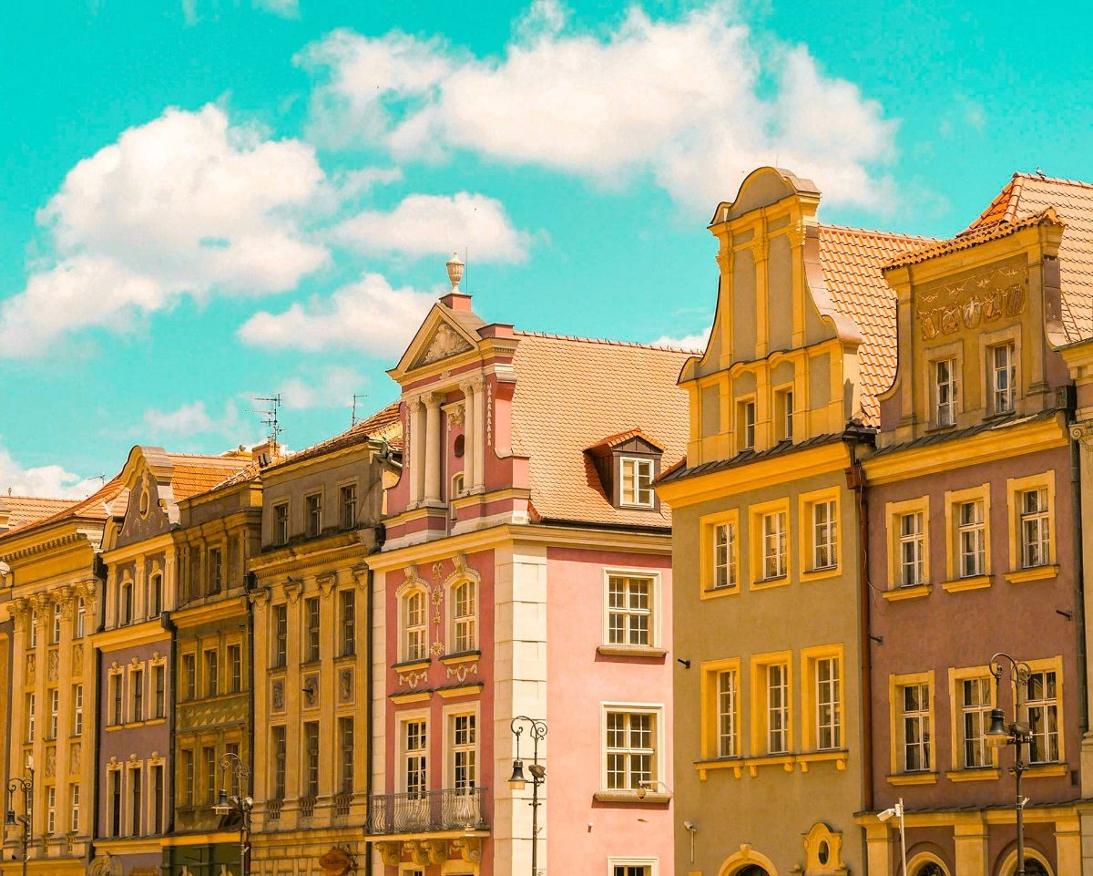 A row of pastel old-town facades in pink and yellow under a turquoise sky with white clouds, edited with the Wes Anderson presets